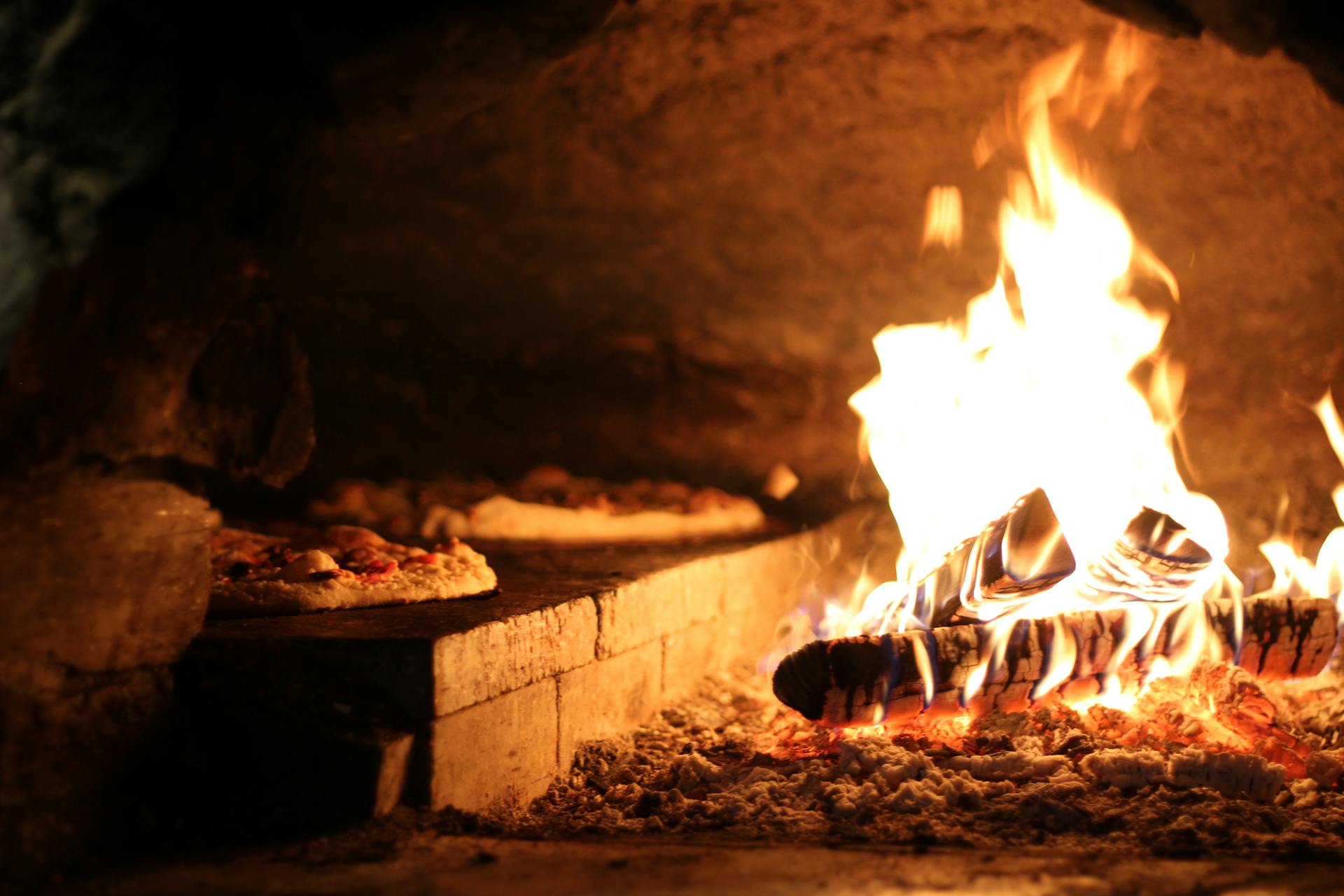 Four à bois napolitain en pleine cuisson, flammes orangées · Cheer Mamma Cannes